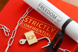 Red book containing Strictly Confidential data, with unlocked padlock and chain and a Freedom of Information Act legal document, which permits public access access to much previously Strictly Confidential information.