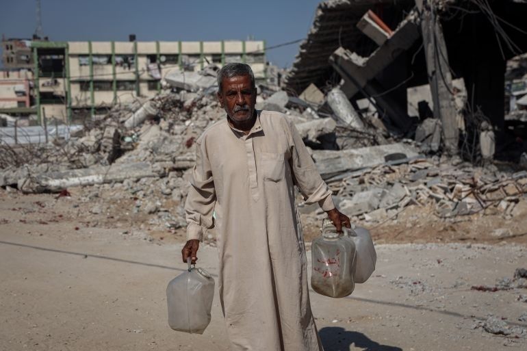 Man carrying water containers past a heavily damaged urban building