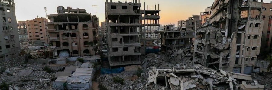 Heavily damaged urban buildings and rubble surrounding makeshift shelters